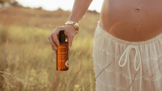pregnant woman walking through a sunny field with vitamin C body oil