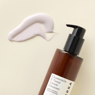 A bottle of Apoterra Chamomile & Tansy Cream Cleanser with a smear of the product texture on a beige background