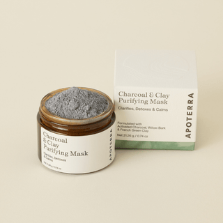 An open jar of Apoterra Charcoal & Clay Purifying Mask next to its product box, showing the gray mask inside, on a warm beige background.