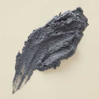 A gray blue textured smear of charcoal and clay mask on a white background