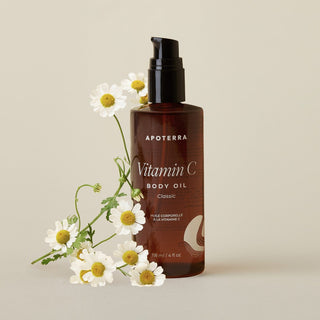 Apoterra Vitamin C Body Oil with chamomile flowers on a beige background