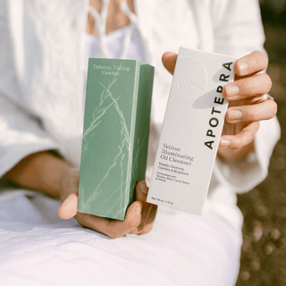 Close-up of a woman's hands holding a box of Apoterra Vetiver Oil Cleanser in an outdoor setting.