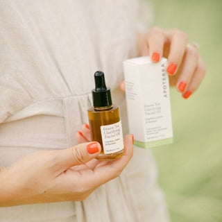 Apoterra Green Tea Clarifying Facial Oil and box close up of hands holding both with orange coral nails