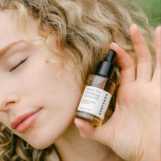 Apoterra Green Tea Clarifying Facial Oil held by blonde woman with clear skin and curly hair