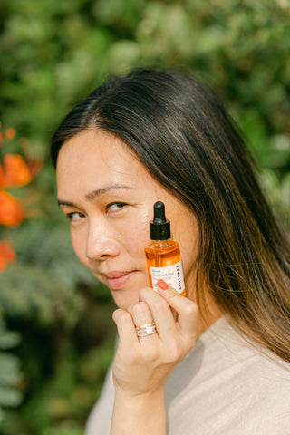 A woman hold a bottle of Apoterra Rose Nourishing Facial Oil up to her face showing beautiful, vibrant hue of the oil
