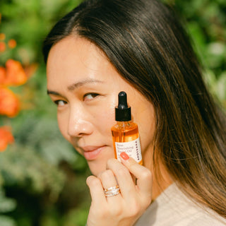 Apoterra Rose Nourishing Facial Oil held by women sunkissed by sunlight and flowers in the background