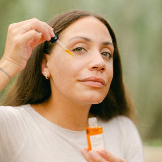 Women applying Apoterra Rose Nourishing Facial Oil to her face using the glass dropper and holding the bottle
