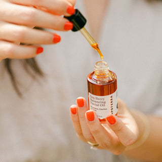 Dropper being held above Apoterra Sea Berry Balancing Facial Oil showing vibrant hue of the oil