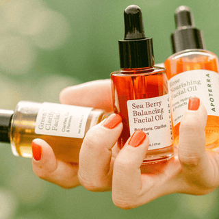 A woman's hand holding all three Apoterra organic natural facial oils in a natural outdoor setting