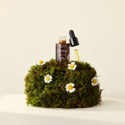 Herbal Clarifying Facial Oil by Apoterra sits on a moss block with flowers. The dropper top is off and shows the herbal oil. 