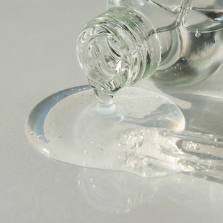 Hyaluronic acid serum texture image dripping from bottle in a pool of clear liquid