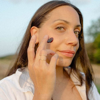 Model applying Apoterra's Hibiscus Exfoliating Face Mask Mud to cheek for rich texture