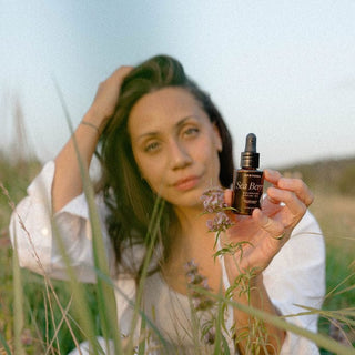 Model holding Sea Berry Balancing Facial Oil bottle by Apoterra in field of wild flowers