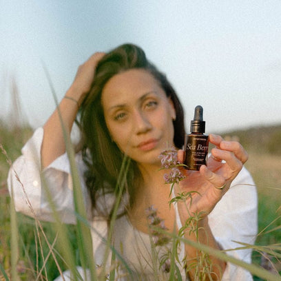 Model holding Sea Berry Balancing Facial Oil bottle by Apoterra in field of wild flowers
