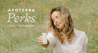 A woman with blonde curly hair in a field of flowers shows an Apoterra facial oil box with text overlaid "Apoterra Perks Loyalty and Rewards"