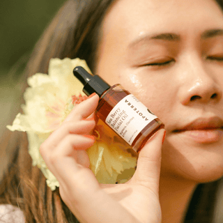 Close up of a woman with a large peony flower near her face, holding Apoterra sea berry balancing oil