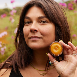 Woman holding a jar of Vitamin C Regenerative Balm in a field with flowers