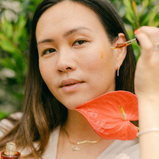 Woman applying Apoterra Sea Berry Balancing Facial Oil with tropical coral flower resting under her face
